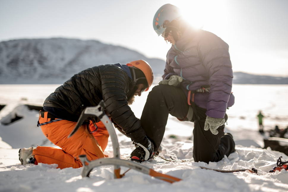 A guide helping a guest getting ready to go ice climbing in Greenland
